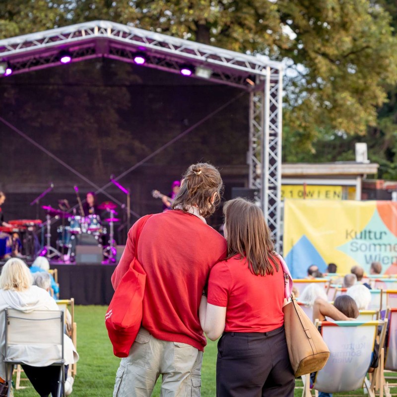 Foto: Judith Stehlik Zwei Personen stehen dicht nebeneinander vor der Kultursommer-Bühne beim Fußballverein 1210. 