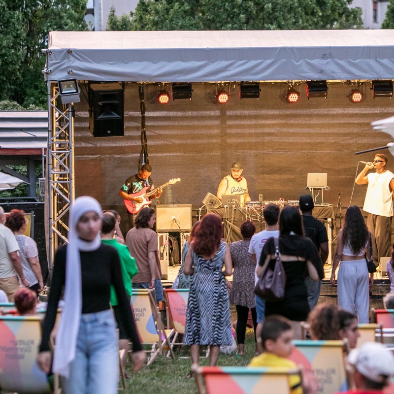 Foto: Judith Stehlik Blick auf die Bühne im Wilhelmsdorfer Park. Das Publikum sitzt in Liegestühlen und steht vor der Bühne. Auf der Bühne sieht man Rapper Maydo.