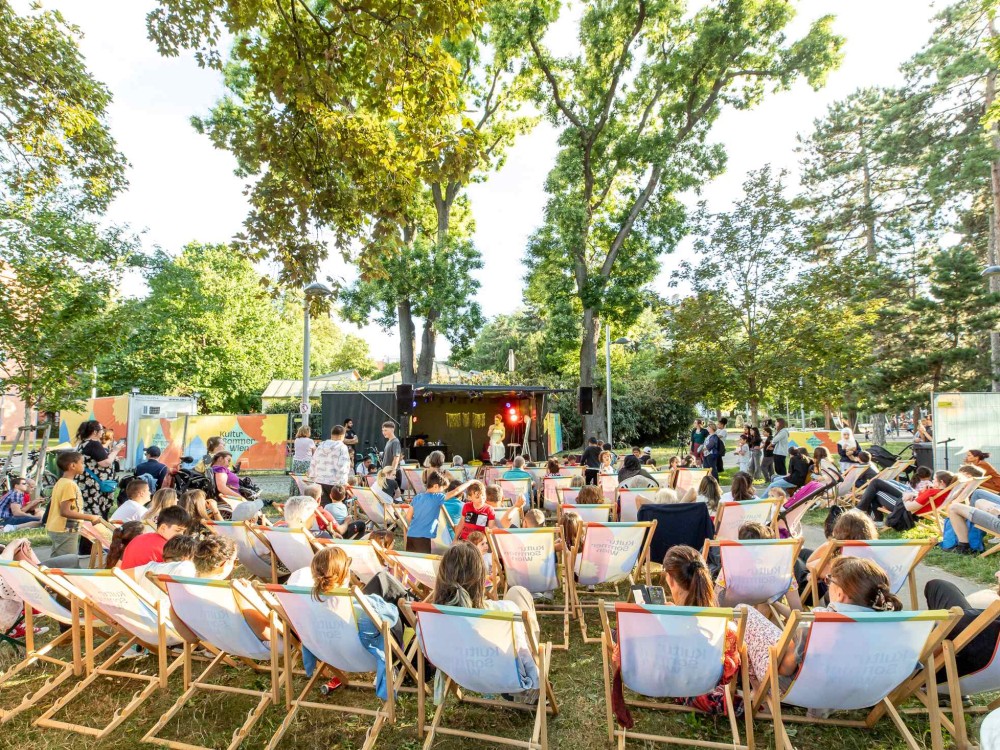Auftritt von Meo auf der Bühne im Hyblerpark. Man sieht das Publikum von hinten in Liegestühlen sitzend.