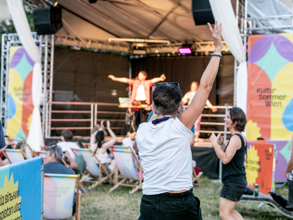 Euroteuro performt beim Kultursommer Wien. Eien Person hebt einen Arm in die Luft. 