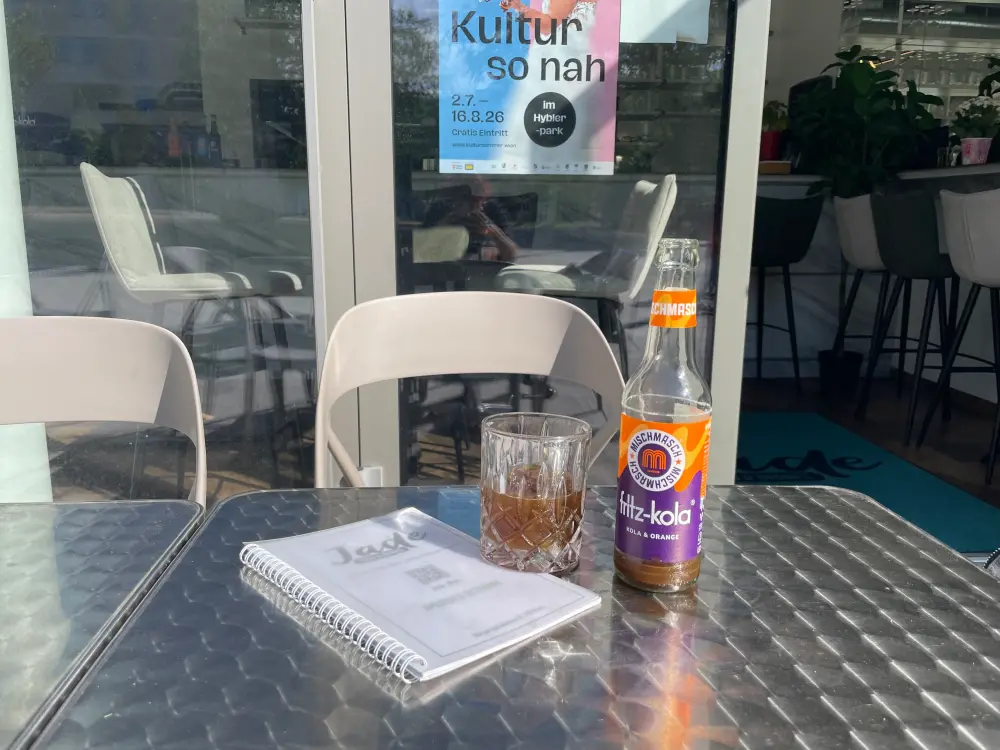 Eine Cola und ein Glas mit Eiswürfel stehen auf einem silbernen Tisch. 