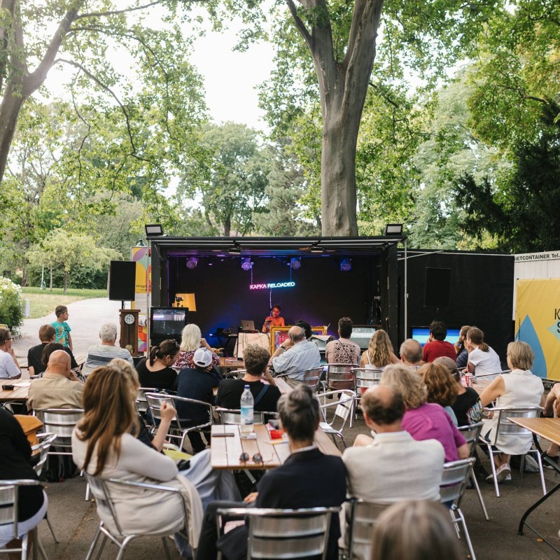 Foto: Judith Stehlik Stanislaus Dick auf der Kultursommer-Bühne im Kongreßpark. Das Publikum sitzt an kleinen Tischen. 