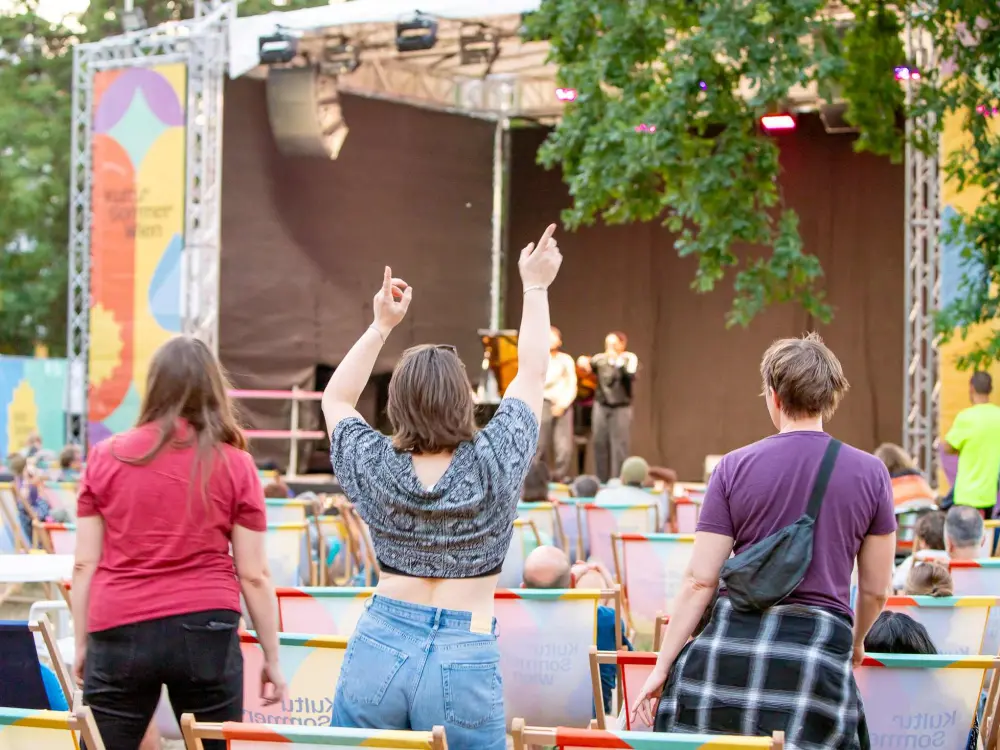 Zwei Personen im Publikum sind beim Konzert von EsRap & Marino Formenti aufgestanden und tanzen. Eine Personen wirft die Arme in die Höhe.