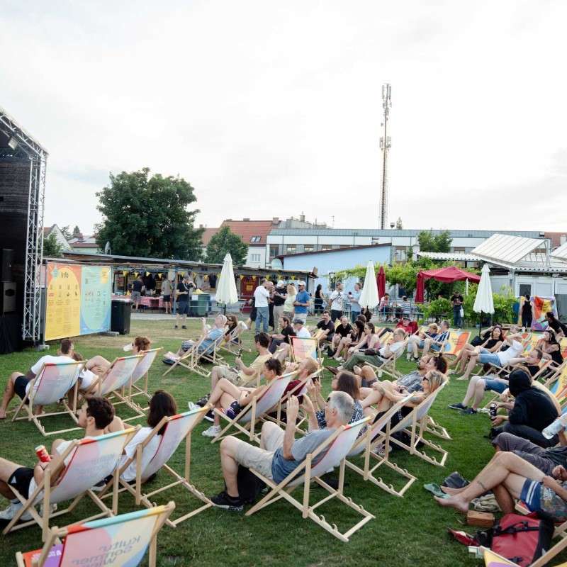 : Vor der Kultursommer-Bühne beim Fußballverein 1210 sitzen Menschen in Liegestühlen. 