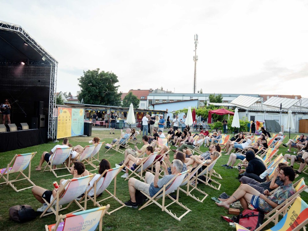 Vor der Kultursommer-Bühne beim Fußballverein 1210 sitzen Menschen in Liegestühlen. 