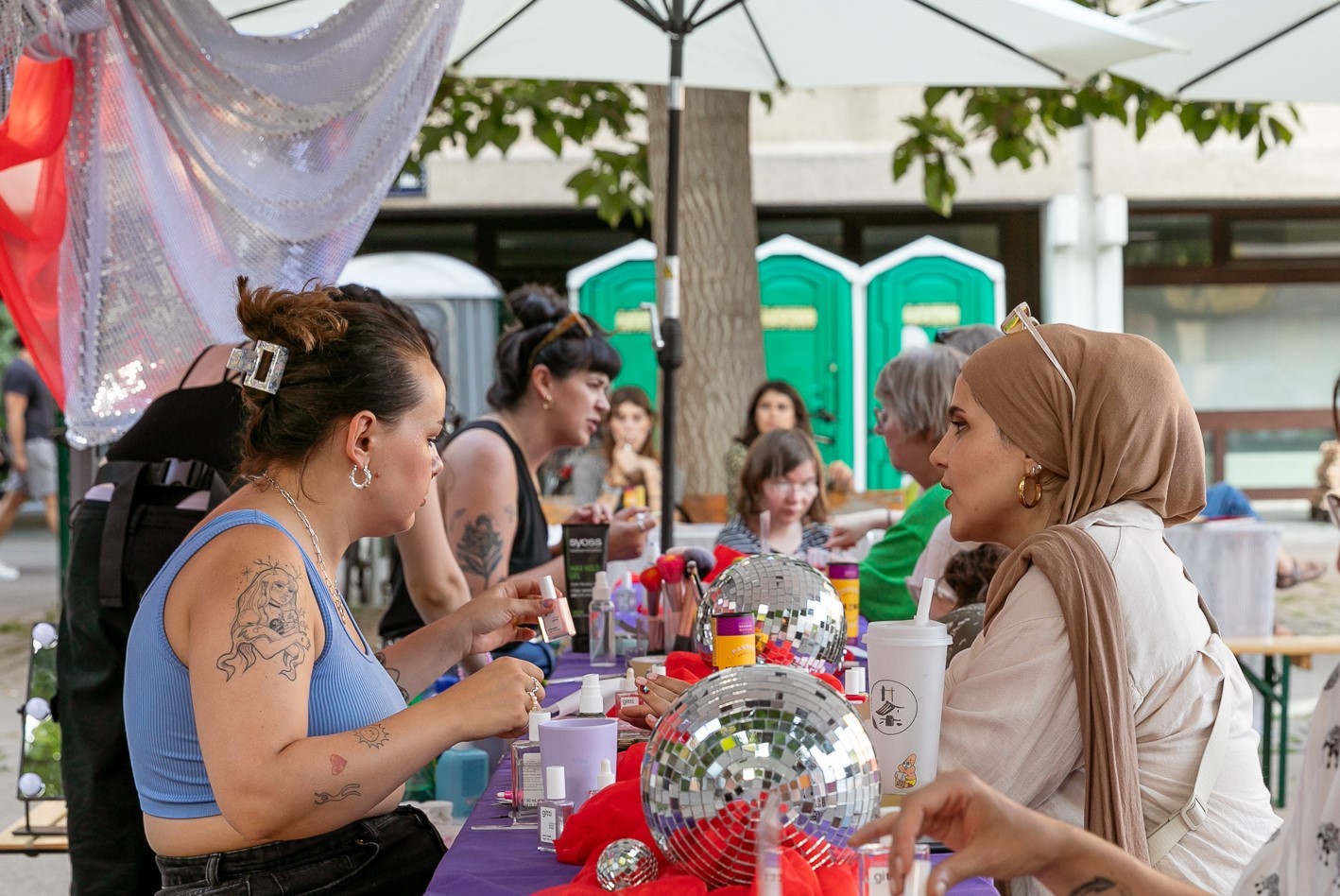 Zwei Frauen sitzen an einem Tisch einander gegenüber. Die eine macht der anderen die Nägel. Es handelt sich um die Styling Corner am Schrödinger Platz im Rahmen von Kultursommer Plus.