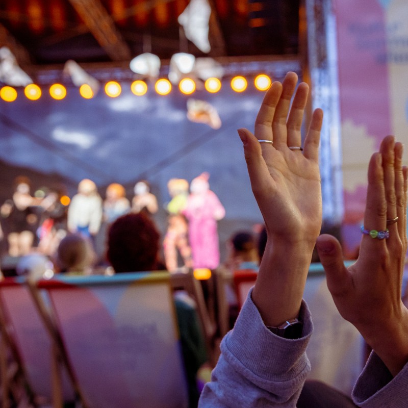 Eine Person klatscht in die Hände, dahinter die Silhouetten der Performer:innen von House of Clits.