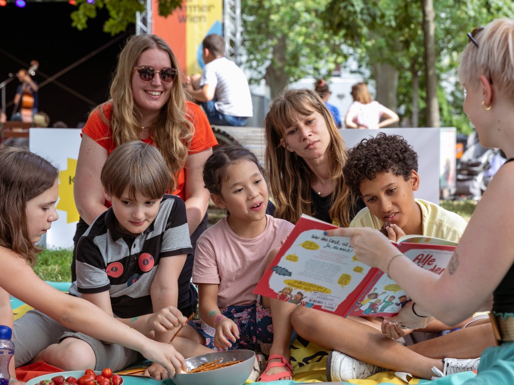 Kinder schauen beim Picknick im Mortarapark gemeinsam in ein Buch. 