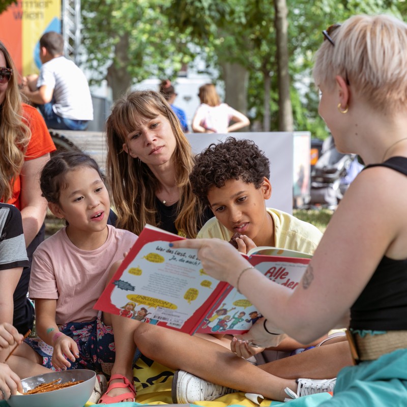 Kinder schauen beim Picknick im Mortarapark gemeinsam in ein Buch. 