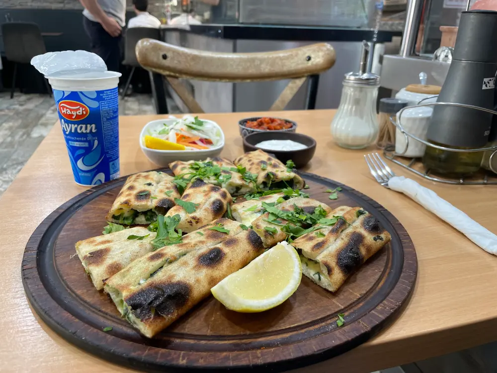 Pide mit Spinat, Ayran und Saucen stehen auf einem Tisch. 