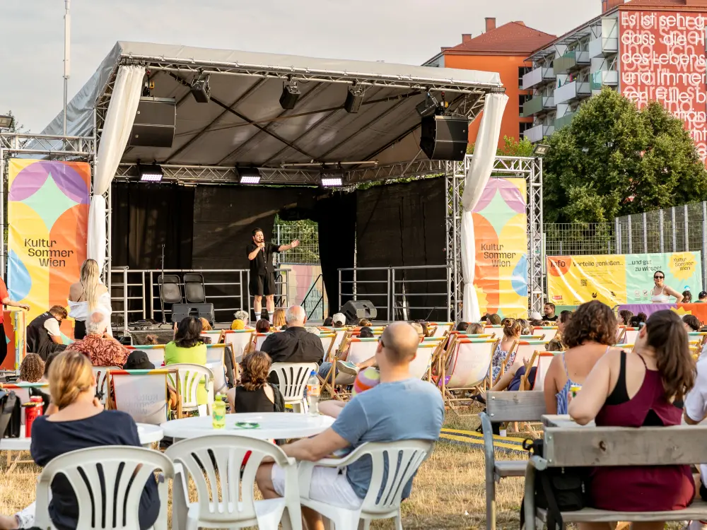 Der Comedian Der Kuseng steht auf einer Bühne vor einem Publikum.