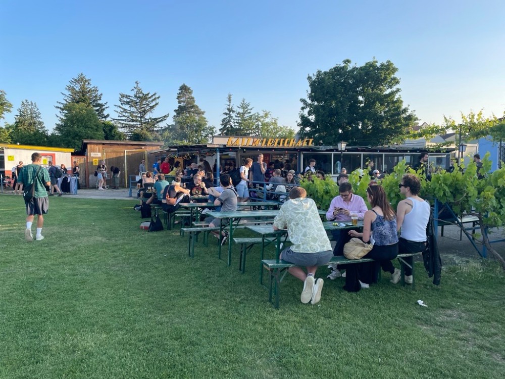 Menschen sitzen im Grünen auf Bierbänken