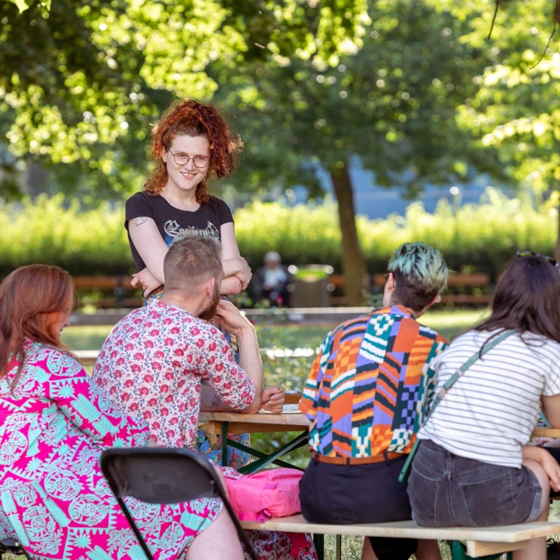 Workshop-Teilnehmende sitzen um einen Tisch. Nathalie Rettenbacher erzählt über die Kunst des Kabaretts. 